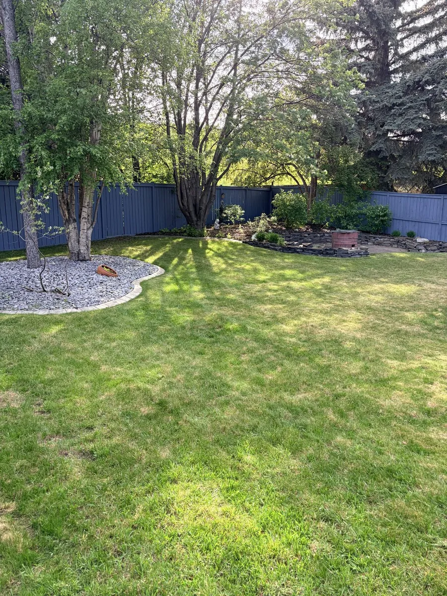 Manicured backyard with mowed lawn, rock garden, and fire pit by Edge Property Services — Calgary